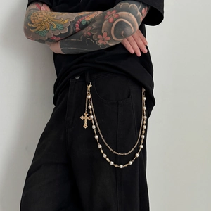 Detail of vintage gold layered pants chain with pearls and cross pendant on black clothes
