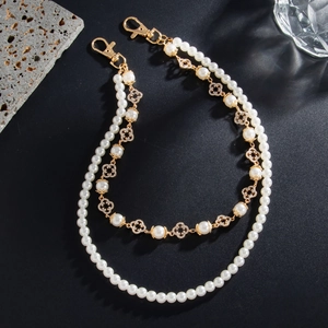Macro detail of double-strand pearl pant chain with golden clover charms and rhinestones