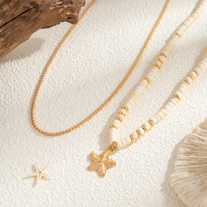 Close-up of double-layer beaded necklace with golden starfish pendant on beach setup