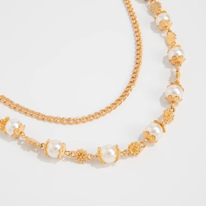Close-up of double-layer gold chain with white pearls and flower charms on white background