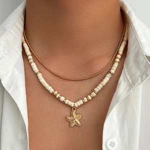 Detail of layered gold chain and white beaded necklace with textured starfish pendant