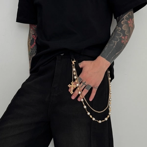 Detail of punk gold pants chain with white pearls and textured cross pendant