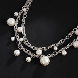 Detail of multi-layer silver metal chain featuring varied size faux pearls and ring charms