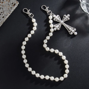 Detail of pearl trousers chain with silver cross pendant on dark background