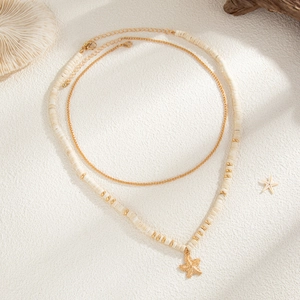 Close-up of a double-layer coconut bead necklace with a gold starfish pendant on white sand
