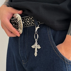 Punk studded leather belt with gothic cross pendant accessory on blue denim jeans