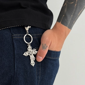 Detailed view of silver cross keychain with gothic relief on blue denim jeans