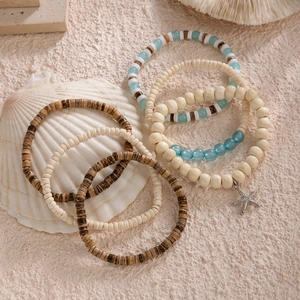 Detail of bohemian coconut shell bead bracelet set with a silver starfish charm on sand