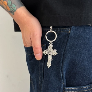Detail of gothic cross keychain with baroque patterns hanging on denim jeans loop