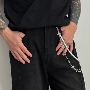 Detail of silver gothic cross chain and white pearl strand on black denim pants