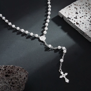 Detailed close-up of a silver iced-out rosary necklace with a cross pendant on volcanic rock