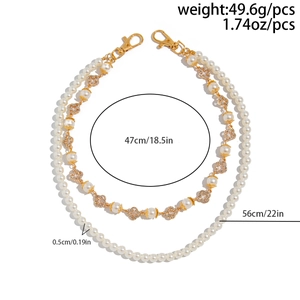 Detail of layered pearl trousers chain with cross charms and lobster clasps on white background