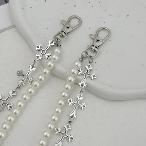 Detail of silver double-layered pants chain with white pearls and metal crosses on a ceramic plate