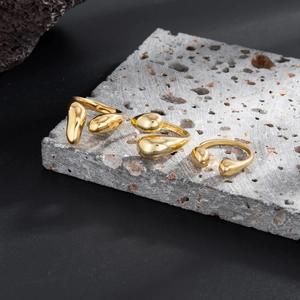 Drei goldene Ringe im Liquid-Drop-Design auf grauem Fels, minimalistischer flüssiger Stil