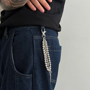 Detail of silver triple-layered beaded wallet chain with cone pendant on blue jeans