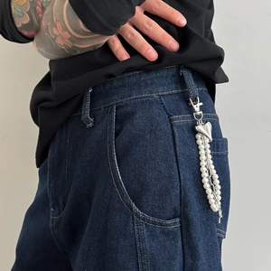 Detail of a pearl heart pendant keychain used as a stylish accessory on denim jeans loops