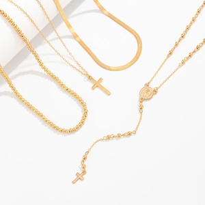 Detail of layered gold cross pendant necklaces with snake and bead chain styles