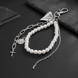 Silver multi-layer keychain with heart and cross pendants and white pearls on rock background