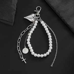Detail of pearl keychain with silver heart, cross pendants and coin on dark stone