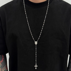 Détail d'un collier chapelet argenté avec pendentif croix sur un t-shirt noir uni