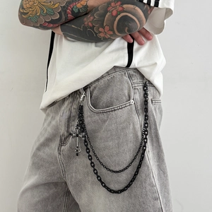 Détail d'une double chaîne de pantalon punk noire avec pendentif croix en strass sur jean