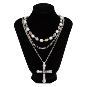 Detail van gelaagde zilveren ketting met kruis, parels en kleurrijke edelstenen op buste