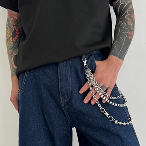 Detail of silver multi-layered metal trousers chain with beads and geometric links on denim