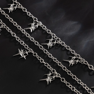 Close-up of multi-layer silver pants chain with star and cross charms on black background