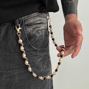 Detail of hip hop gold metal trouser chain with black and white pearls on grey denim