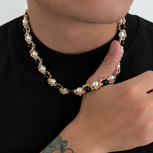 Detail van de gouden gedraaide touwketting met witte parels en zwarte kralen om de nek