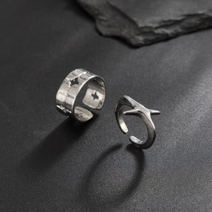 Close-up of industrial silver rings with hollow cross stars on a dark stone background