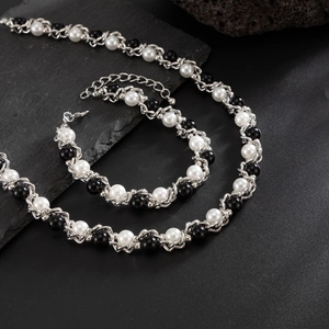 Detail van de zilveren vlechtketting met zwarte en witte parels op een donkere steen