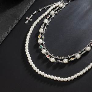 Detailed view of multilayered pearl chain with cross pendant on dark stone background
