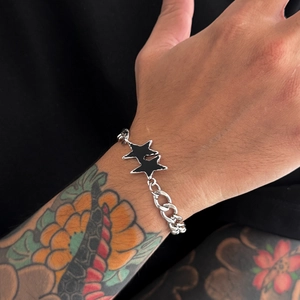 Dettaglio del bracciale a catena cubana d'argento con ciondoli a stella nera su polso tatuato