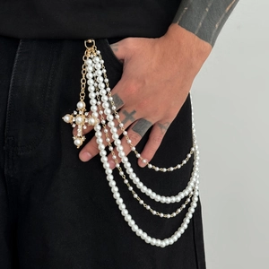 Detailed close-up of layered pearl waist chains with crystal cross pendant on denim