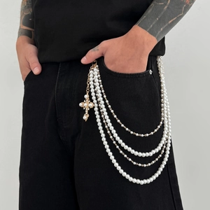 Detail of layered pearl trousers chain with gold cross pendant on black denim jeans