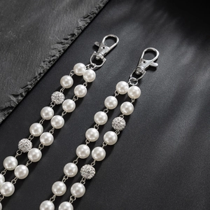 Close-up of pearl chain with rhinestone balls and silver lobster clasp on black stone