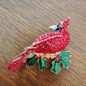 Sparkling cardinal bird brooch with red rhinestones and green holly leaves on wood surface