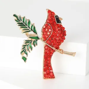 Broche oiseau cardinal rouge étincelant avec feuilles en émail vert sur branche