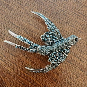 Macro shot of silver swallow brooch with dark rhinestones on a wooden background