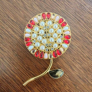 Dettaglio della spilla a fiore con perle bianche, cristalli e petali in gemma rossa