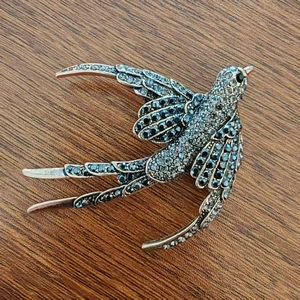 Detailed macro view of a vintage silver swallow brooch with blue and white crystals