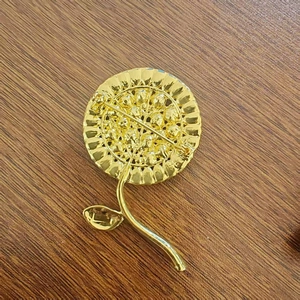 Vista posteriore della spilla a girasole dorata con strass e perle su tavolo di legno