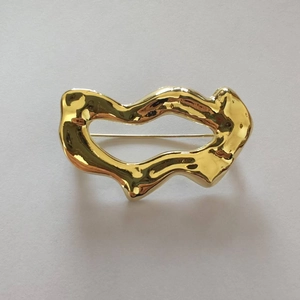 Vue macro d'une broche géométrique creuse dorée avec une surface polie et ondulée