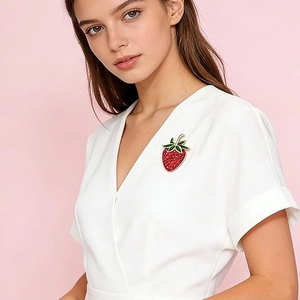 Sparkling red strawberry brooch with green enamel leaves on white V-neck garment
