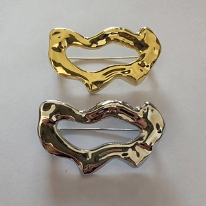 Détail de broches géométriques ondulées ajourées en finitions métal doré et argenté poli