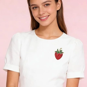 Creative strawberry brooch with red rhinestones and green leaves worn on white blazer
