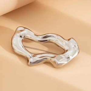 Broche géométrique argentée creuse avec texture ondulée sur fond pêche chaud