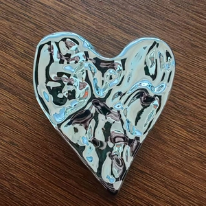 Macro detail of silver liquid metal heart brooch with hammered 3D fluid texture on wood