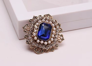 Details einer Vintage Goldbrosche mit großem blauem Kristall und Perlenumrandung